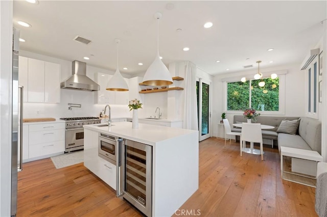 kitchen featuring wall chimney range hood, beverage cooler, high end stove, modern cabinets, and white cabinets