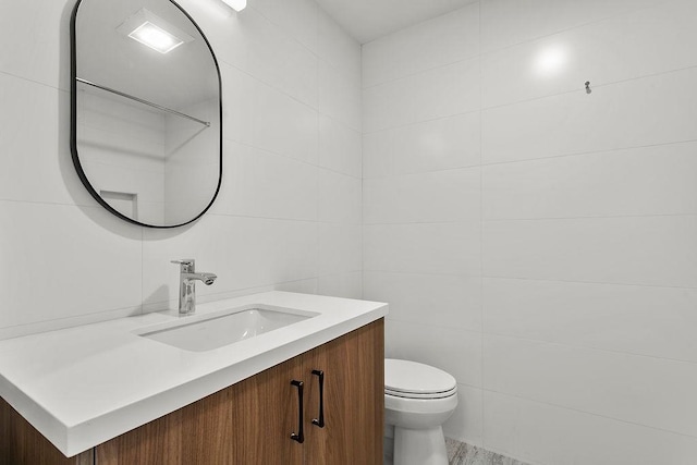 half bathroom featuring vanity, toilet, and tile walls