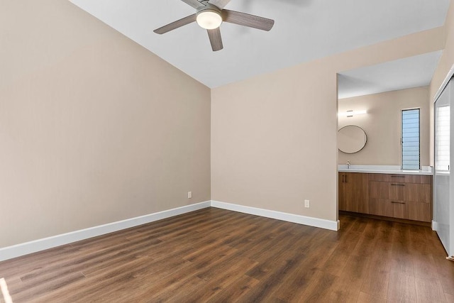 unfurnished bedroom with baseboards, ceiling fan, dark wood-type flooring, a sink, and vaulted ceiling