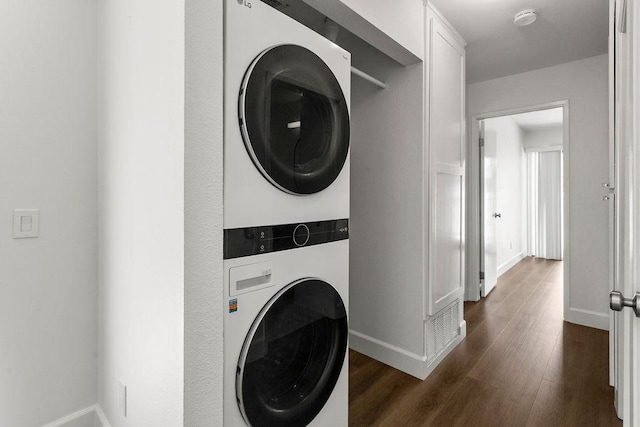 washroom featuring laundry area, stacked washer and clothes dryer, dark wood-style flooring, and baseboards