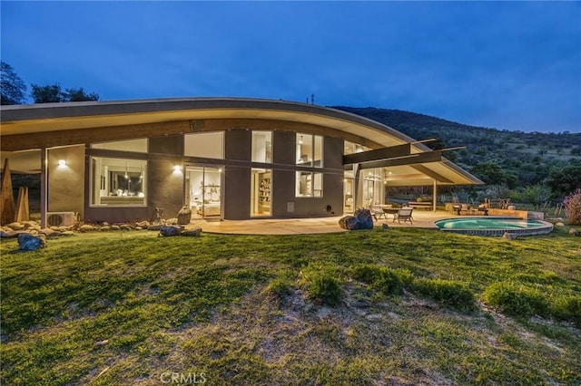 rear view of house with a patio area, an outdoor pool, a mountain view, an in ground hot tub, and stucco siding