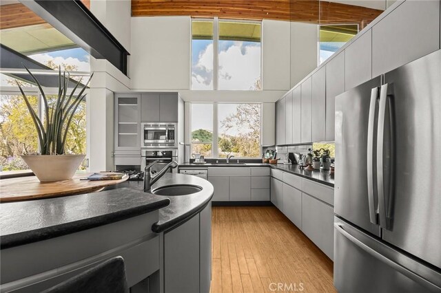 kitchen featuring dark countertops, a sink, light wood-type flooring, gray cabinets, and appliances with stainless steel finishes