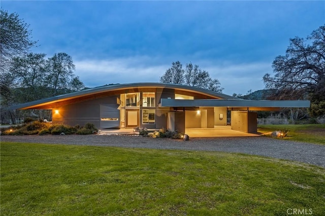 back of property featuring an attached carport, a yard, and curved driveway