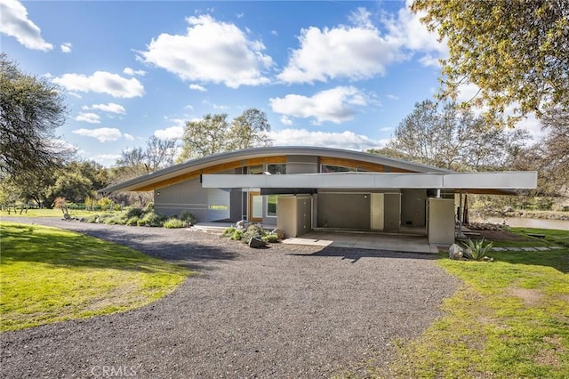 view of front of home featuring stucco siding, gravel driveway, an attached carport, and a front lawn
