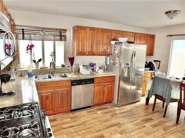 kitchen with a sink, light wood-style floors, brown cabinets, light countertops, and appliances with stainless steel finishes