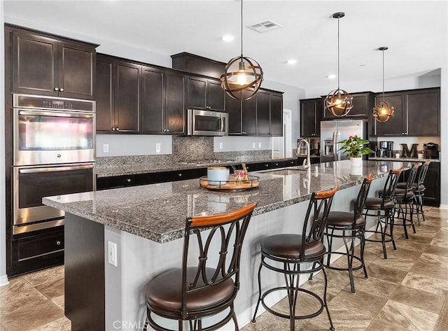 kitchen featuring stainless steel appliances, a sink, a large island with sink, hanging light fixtures, and dark brown cabinets