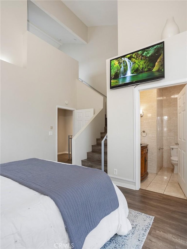 bedroom featuring a towering ceiling, wood finished floors, and ensuite bathroom