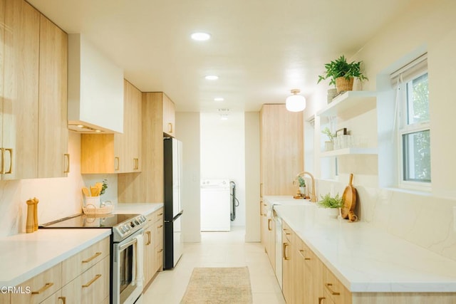 kitchen featuring stainless steel electric stove, light brown cabinetry, freestanding refrigerator, washer / dryer, and recessed lighting