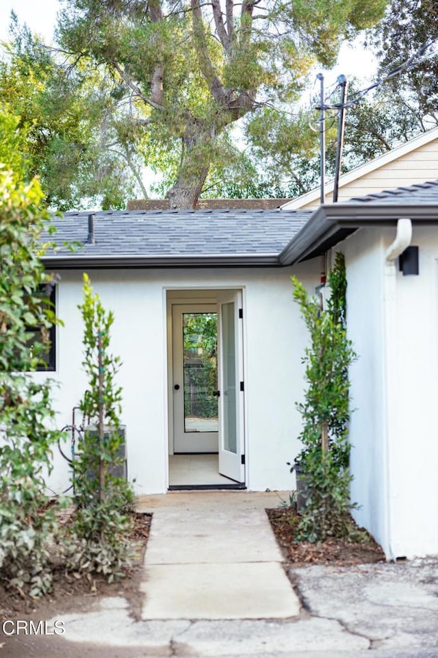 entrance to property with stucco siding and a shingled roof
