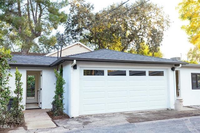 view of front of property featuring a garage, stucco siding, and roof with shingles