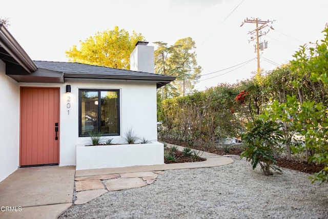 property entrance featuring a chimney and stucco siding