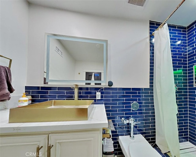 bathroom featuring a tile shower, tile walls, visible vents, and vanity