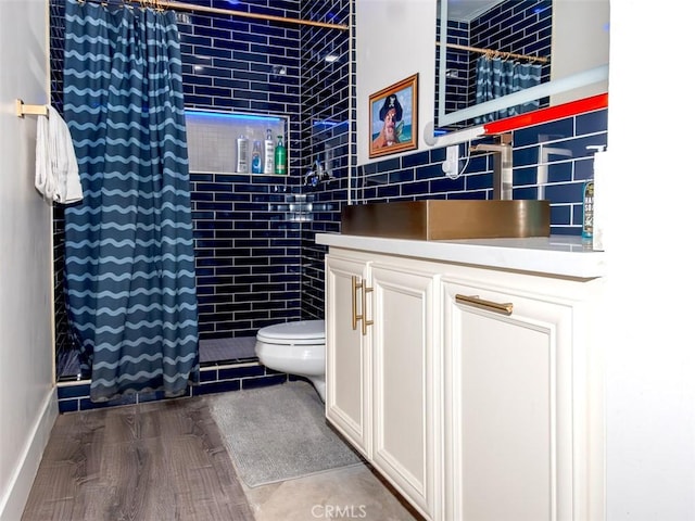 bathroom featuring wood finished floors, toilet, vanity, baseboards, and tiled shower
