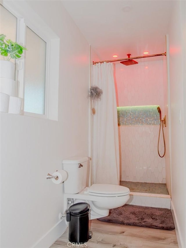 full bathroom with baseboards, toilet, wood finished floors, and tiled shower