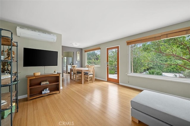 living area with baseboards, a wall unit AC, and light wood-type flooring
