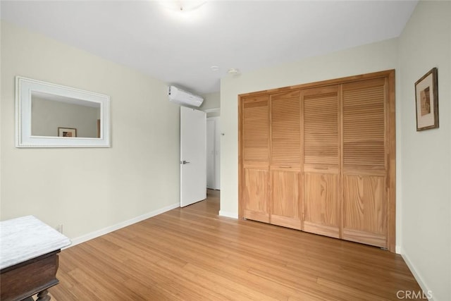 unfurnished bedroom with a closet, a wall mounted air conditioner, baseboards, and wood finished floors