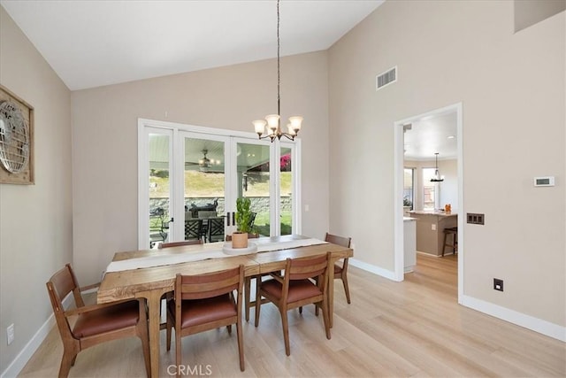 dining space featuring light wood-style flooring, baseboards, visible vents, a notable chandelier, and high vaulted ceiling