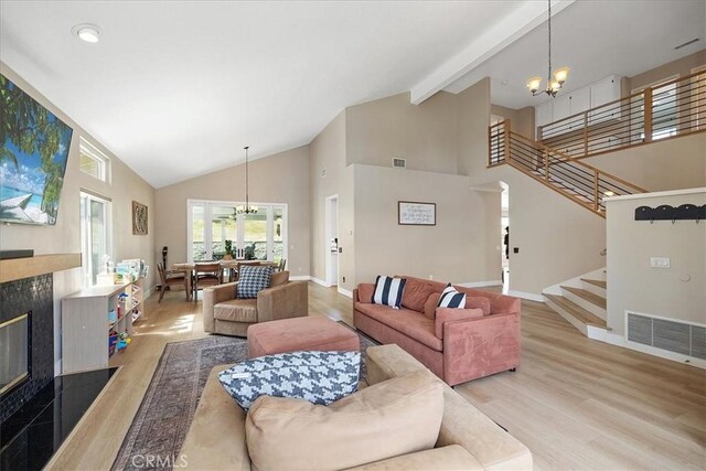 living area featuring high vaulted ceiling, light wood-type flooring, an inviting chandelier, a fireplace, and visible vents