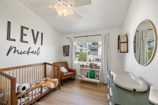 bedroom with light wood-style floors, a crib, and ceiling fan