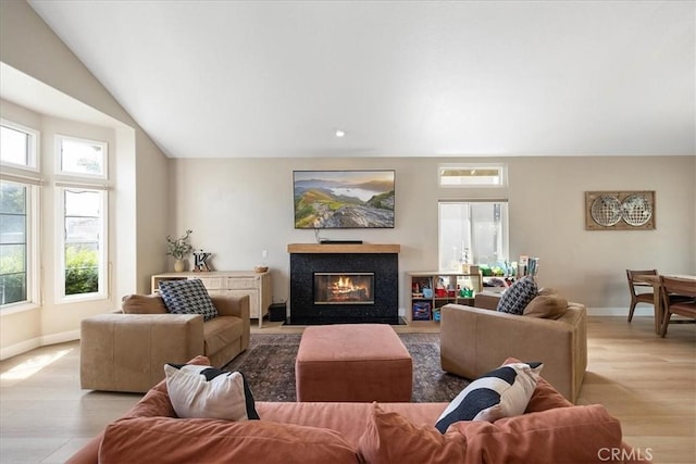 living room with a glass covered fireplace, wood finished floors, a healthy amount of sunlight, and baseboards