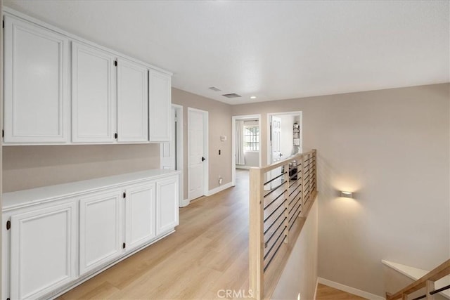 corridor featuring light wood-type flooring, visible vents, baseboards, and an upstairs landing