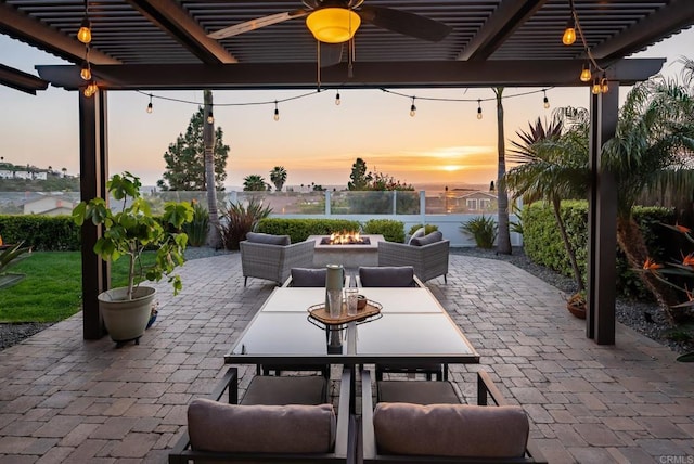 patio terrace at dusk featuring a fire pit, a pergola, outdoor dining area, and ceiling fan