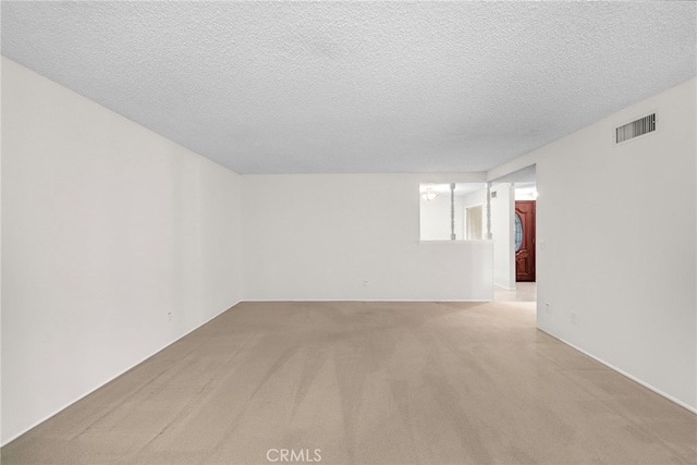 spare room featuring light colored carpet, a textured ceiling, and visible vents