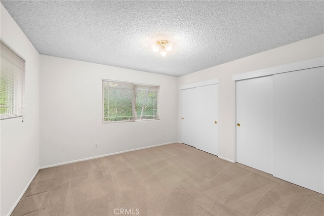 unfurnished bedroom with carpet flooring, a textured ceiling, multiple closets, and baseboards