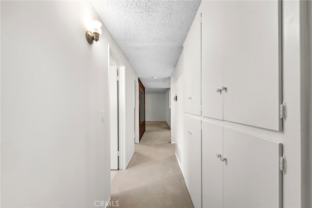 hallway with baseboards, light carpet, and a textured ceiling