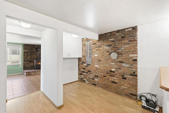 unfurnished room with light wood-style flooring, a wood stove, baseboards, and brick wall