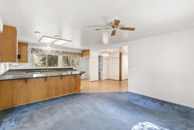 kitchen featuring a peninsula, light carpet, dark countertops, brown cabinets, and a breakfast bar