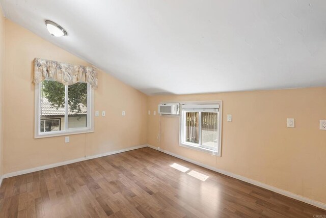 interior space featuring an AC wall unit, vaulted ceiling, wood finished floors, and baseboards