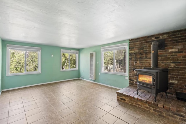 unfurnished living room featuring a wood stove, tile patterned flooring, and baseboards