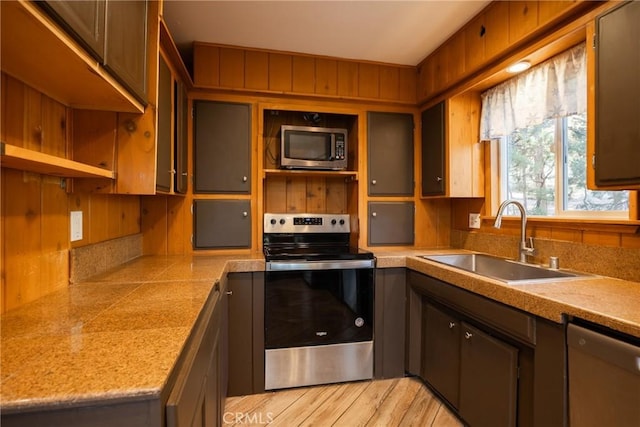 kitchen featuring open shelves, a sink, stainless steel appliances, light wood finished floors, and light countertops