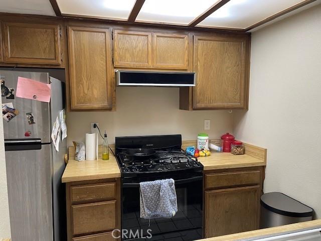 kitchen with extractor fan, black gas range, light countertops, and freestanding refrigerator
