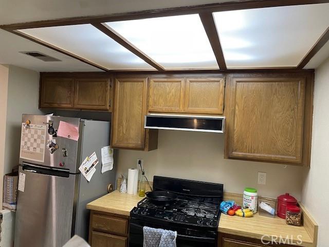 kitchen with light countertops, range hood, black gas range, visible vents, and freestanding refrigerator