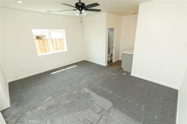 empty room featuring dark colored carpet, visible vents, a ceiling fan, and baseboards