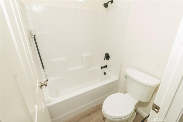 bathroom with baseboards, wood finished floors, washtub / shower combination, and toilet