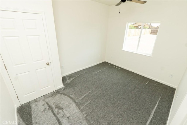 unfurnished room with dark colored carpet, a ceiling fan, and baseboards