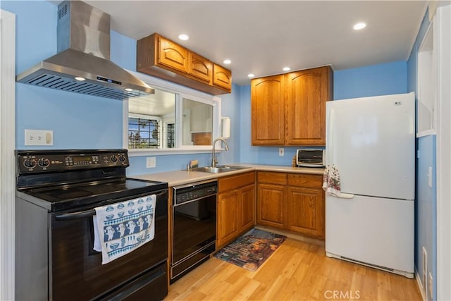 kitchen with a sink, black appliances, brown cabinets, light wood finished floors, and wall chimney exhaust hood