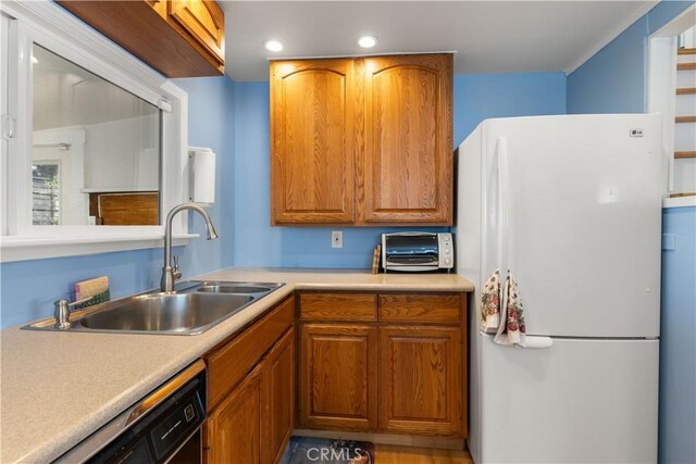 kitchen with brown cabinets, light countertops, a sink, freestanding refrigerator, and black dishwasher