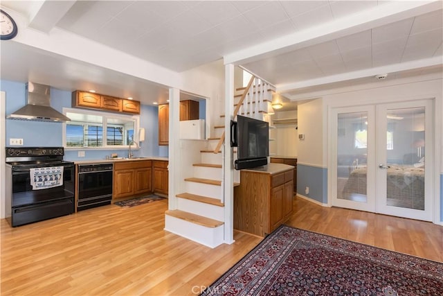 kitchen featuring wall chimney exhaust hood, light wood-style flooring, french doors, brown cabinets, and black appliances