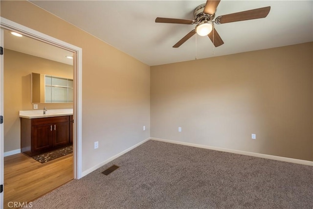 empty room with a sink, ceiling fan, light carpet, baseboards, and visible vents