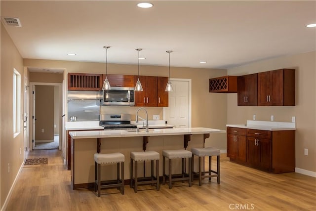 kitchen with a sink, light wood finished floors, baseboards, appliances with stainless steel finishes, and visible vents