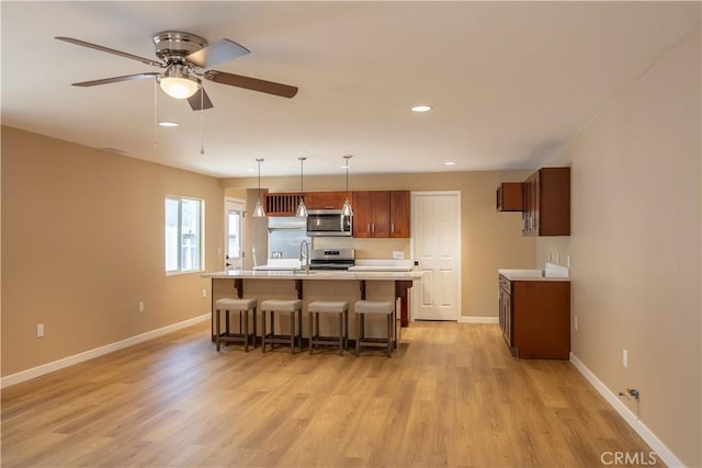 kitchen featuring light countertops, light wood-type flooring, baseboards, appliances with stainless steel finishes, and a breakfast bar area
