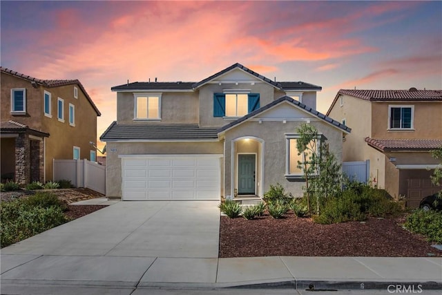 traditional-style home featuring a tile roof, driveway, fence, an attached garage, and stucco siding