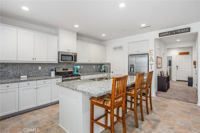 kitchen with a sink, a breakfast bar, stone finish flooring, appliances with stainless steel finishes, and visible vents