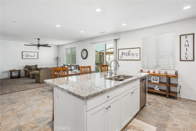 kitchen featuring white cabinets, stainless steel dishwasher, a sink, and stone finish flooring
