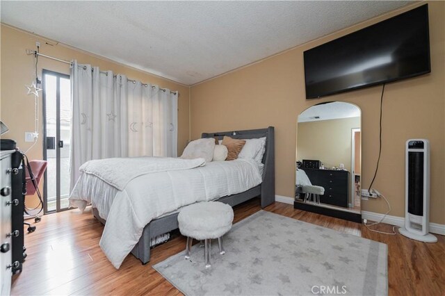 bedroom with arched walkways, wood finished floors, a textured ceiling, and baseboards