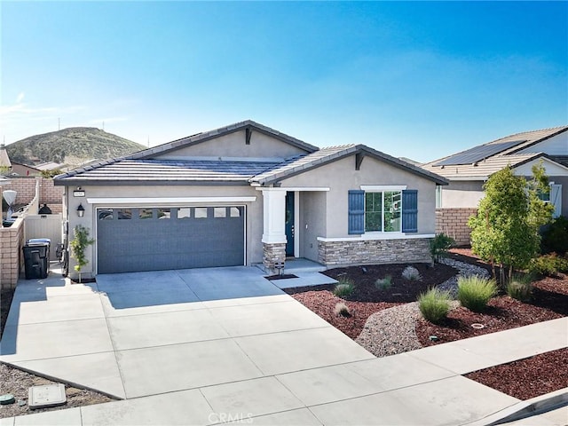 view of front of house with concrete driveway, stone siding, fence, a garage, and stucco siding